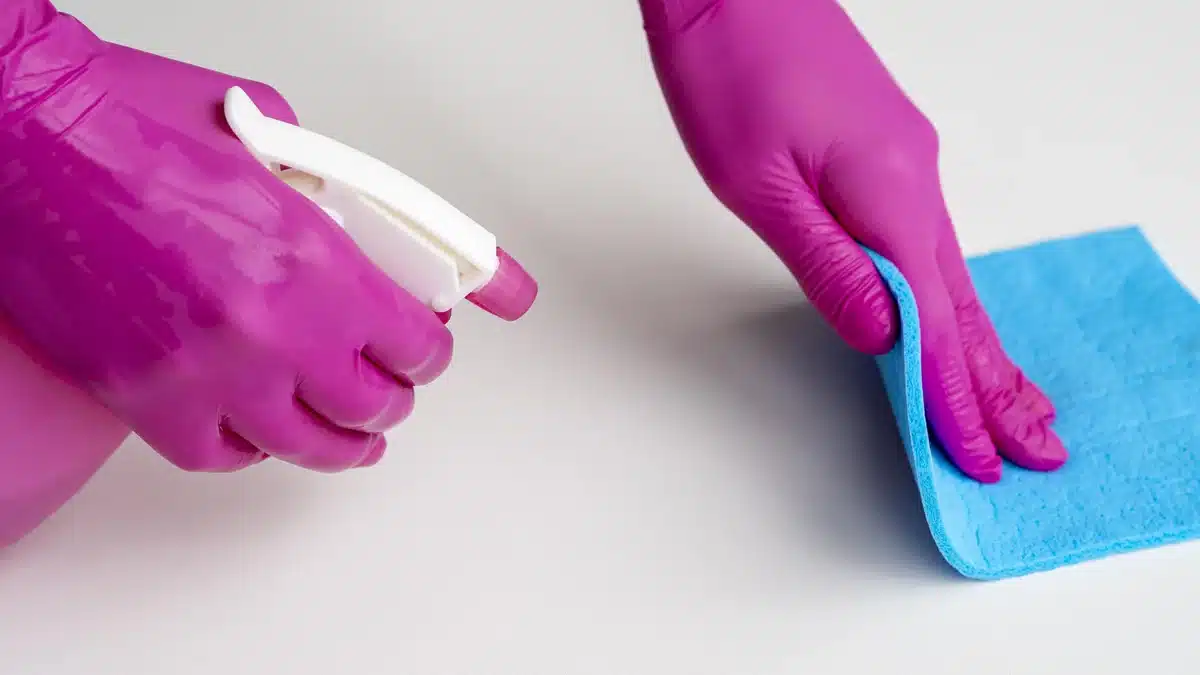 Gloved hands applying a cleaning product to a surface