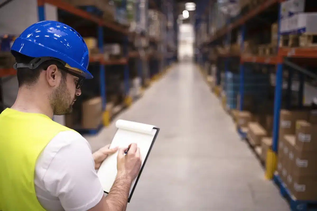 Warehouse worker checking a clipboard beside storage racks
